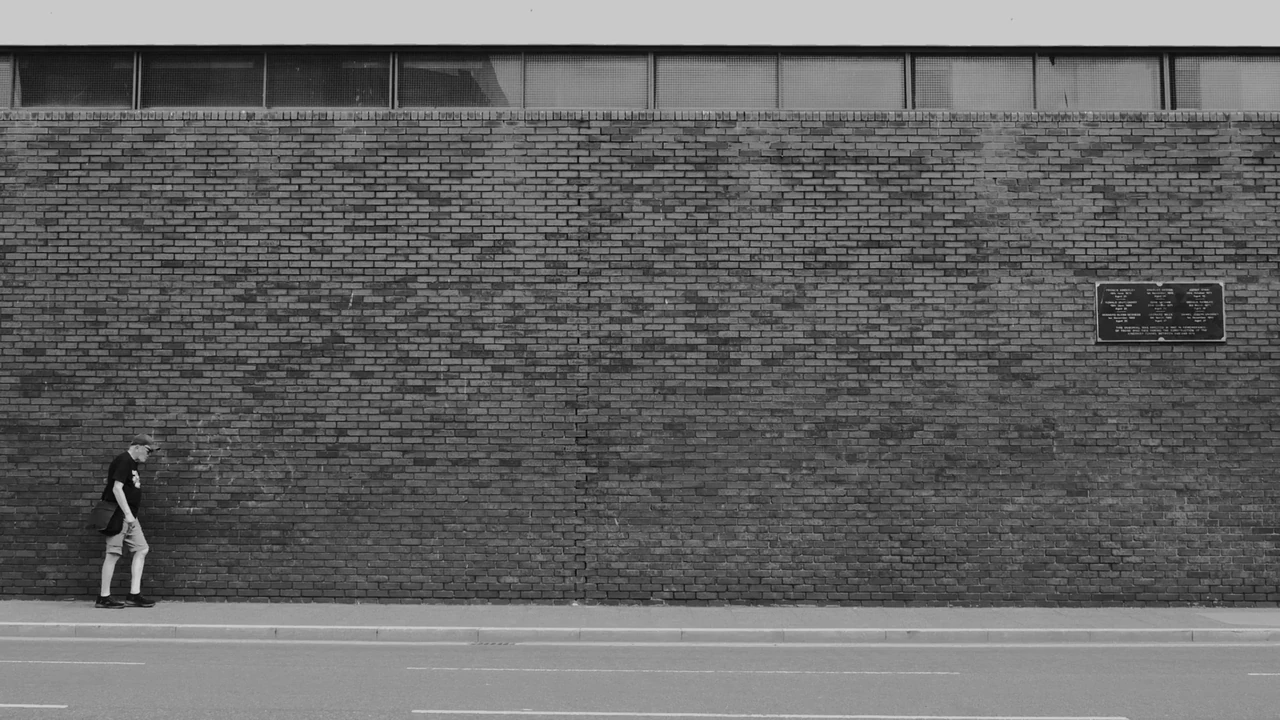 A lone pedestrian passing a long brick wall, in black and white. Photograph by Mark C Grant.