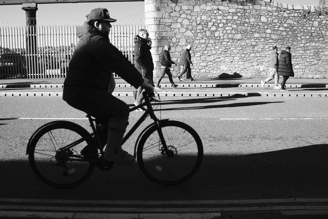 A cyclist passes the sunlit dock wall outside Bramley Moore (Hill Dickinson), Liverpool. Black and white photograph by Mark C Grant.