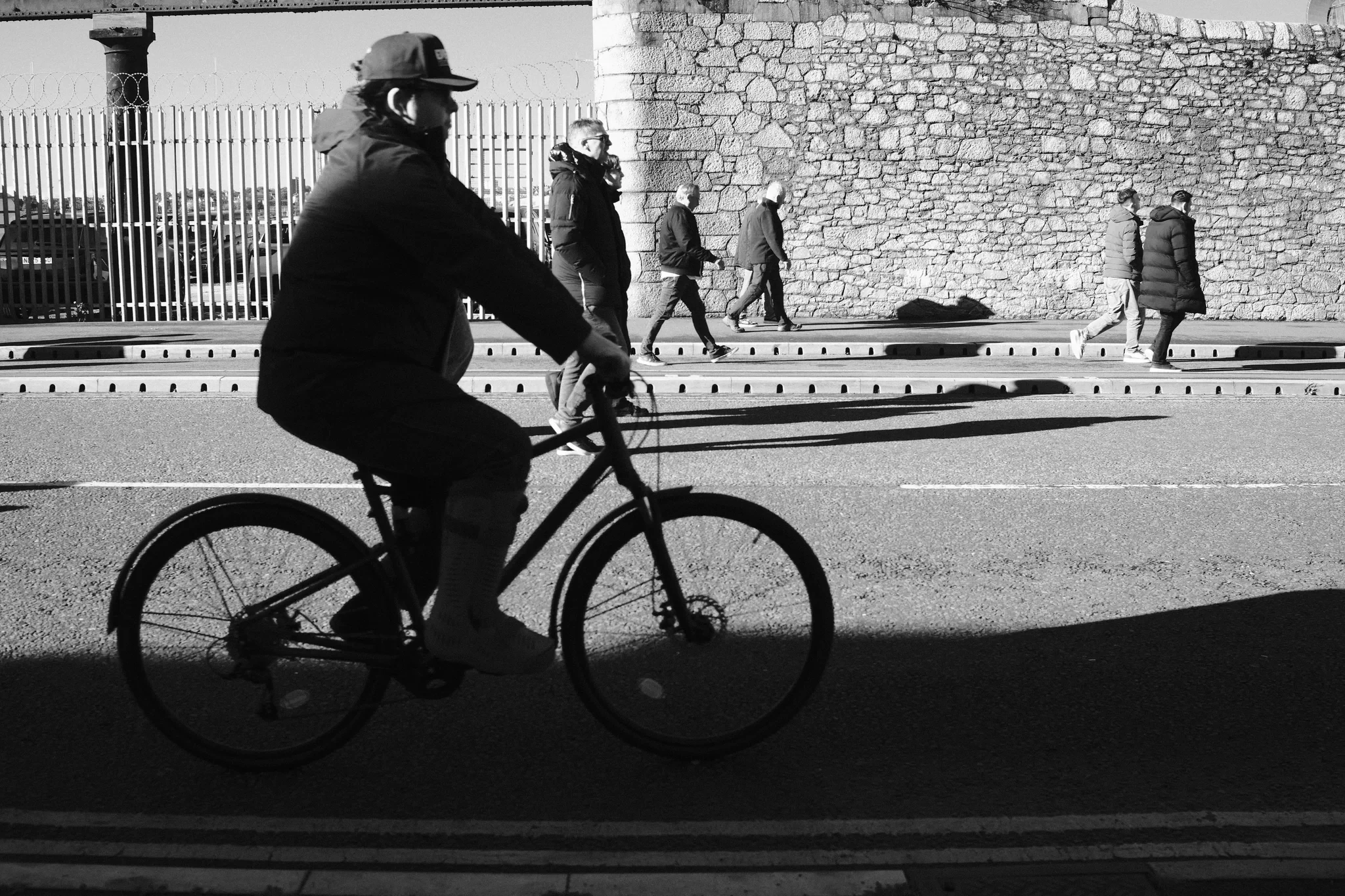 A cyclist passes the sunlit dock wall outside Bramley Moore (Hill Dickinson), Liverpool. Black and white photograph by Mark C Grant.