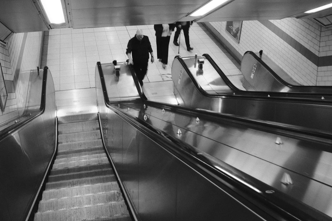 An overhead view of escalators and people moving between levels. Black and white photograph by Mark C Grant.