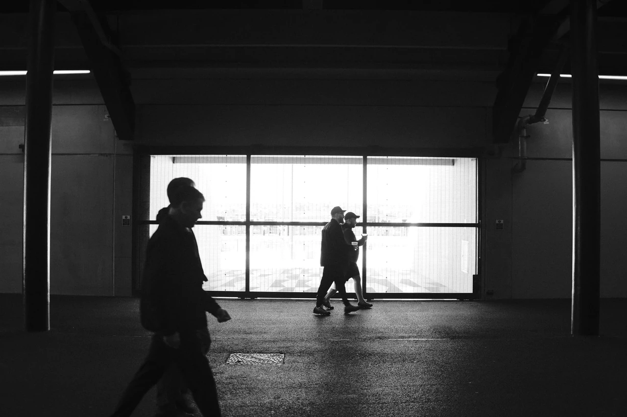 Silhouetted visitors pass a bright opening at Bramley Moore (Hill Dickinson), Everton’s stadium in Liverpool. Black and white photograph by Mark C Grant.