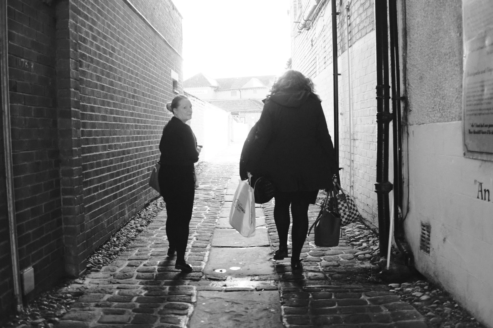 People walking along a cobbled passage towards a bright opening. Black and white photograph by Mark C Grant.