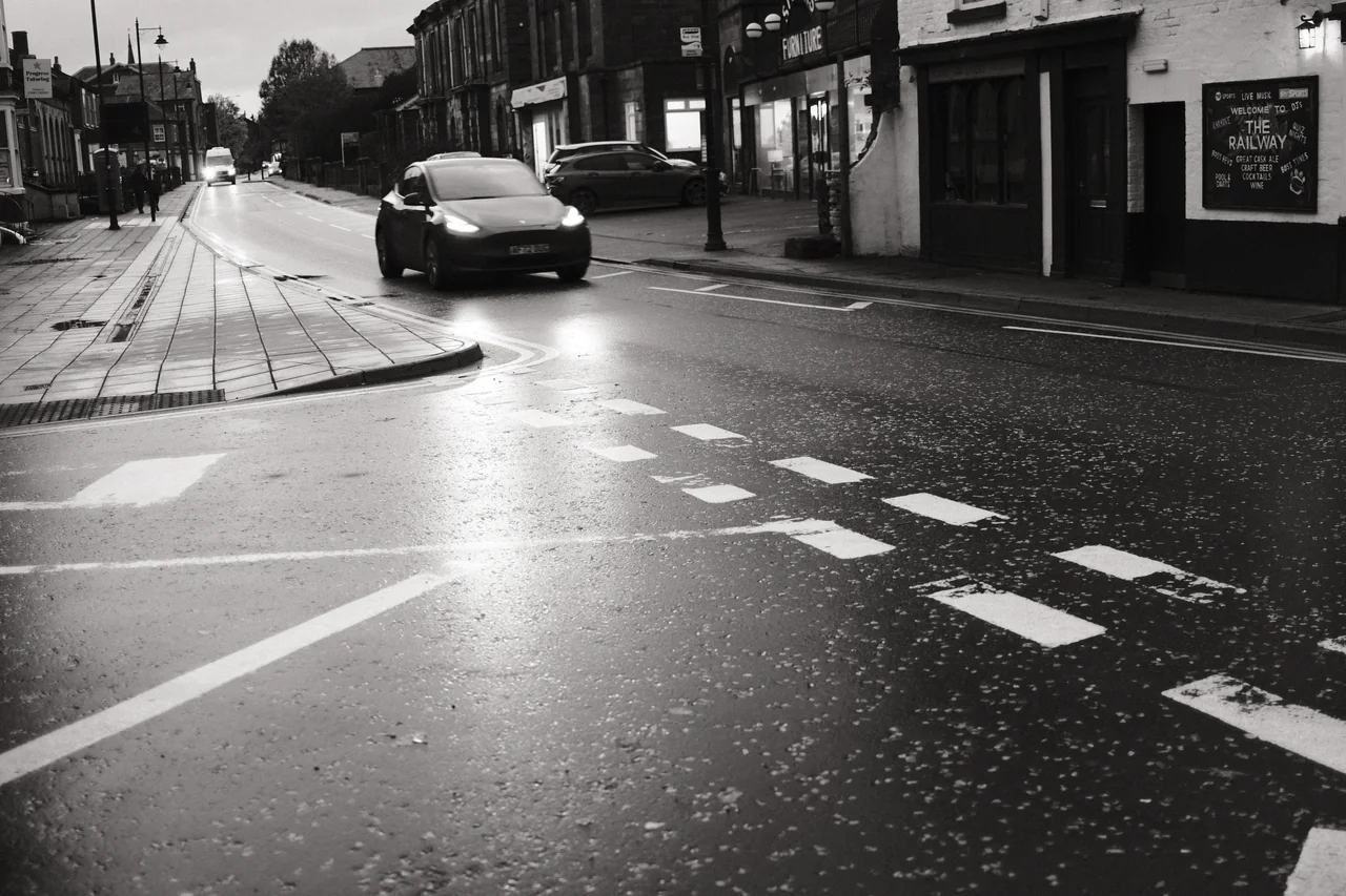 Headlights reflect on the wet road beside The Railway pub on Derby Street in Ormskirk. Black and white photograph by Mark C Grant.