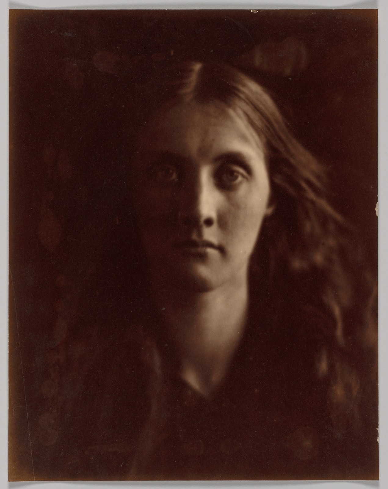 Julia Jackson looks directly towards the camera; one side of her face emerges from deep brown shadow and her loose hair fades into the background.