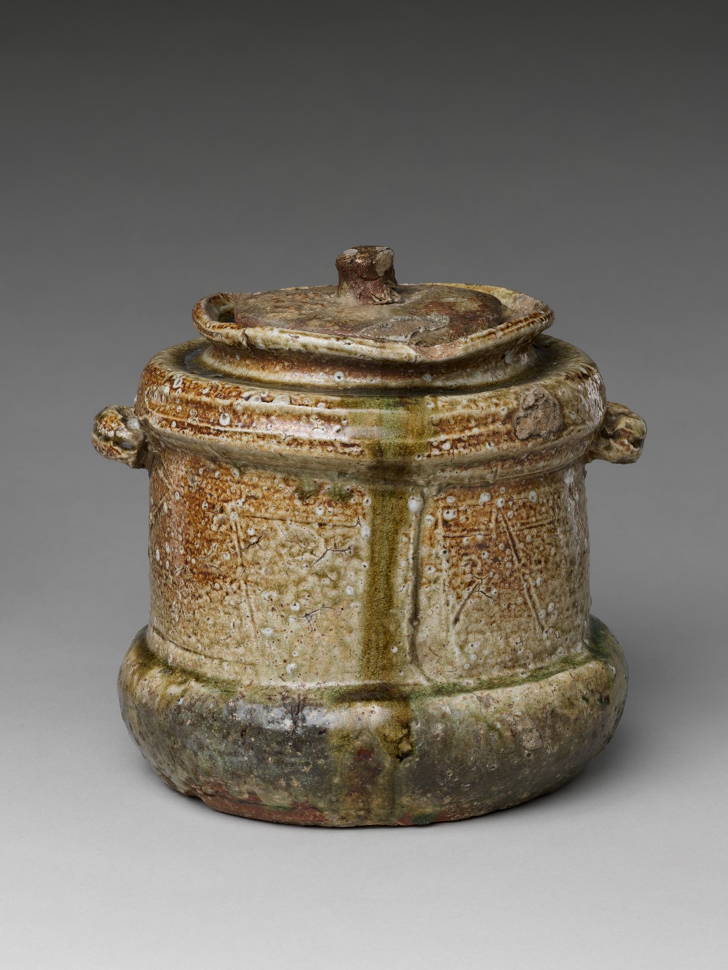 An irregular Iga stoneware water jar with an irregular lid, small side lugs, a rough surface and patches of natural ash glaze.