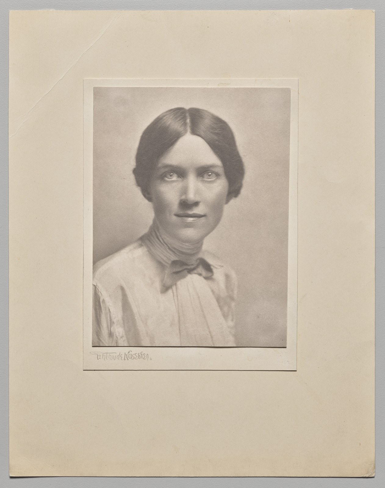 A softly lit bust-length portrait of Honoré Willsie Morrow, wearing a light blouse and looking towards the camera, sits within a large pale paper mount.
