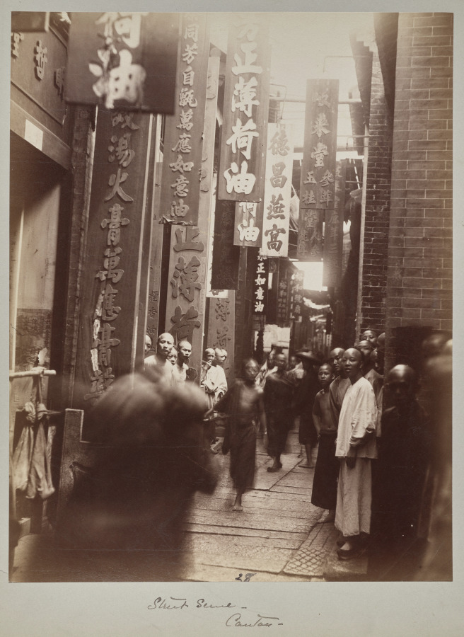Tall shop signs crowd a narrow Guangzhou street; a moving figure blurs across the near left while people beside the shops look towards the camera.