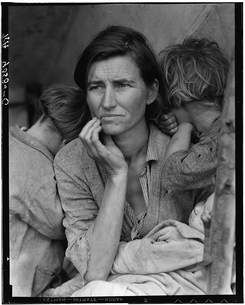 Florence Owens Thompson sits with three children, two turned into her shoulders and a baby on her lap; her hand rises to her cheek as she looks beyond the frame.