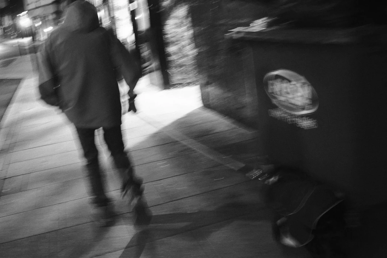 A blurred pedestrian moving past street furniture. Black and white photograph by Mark C Grant.