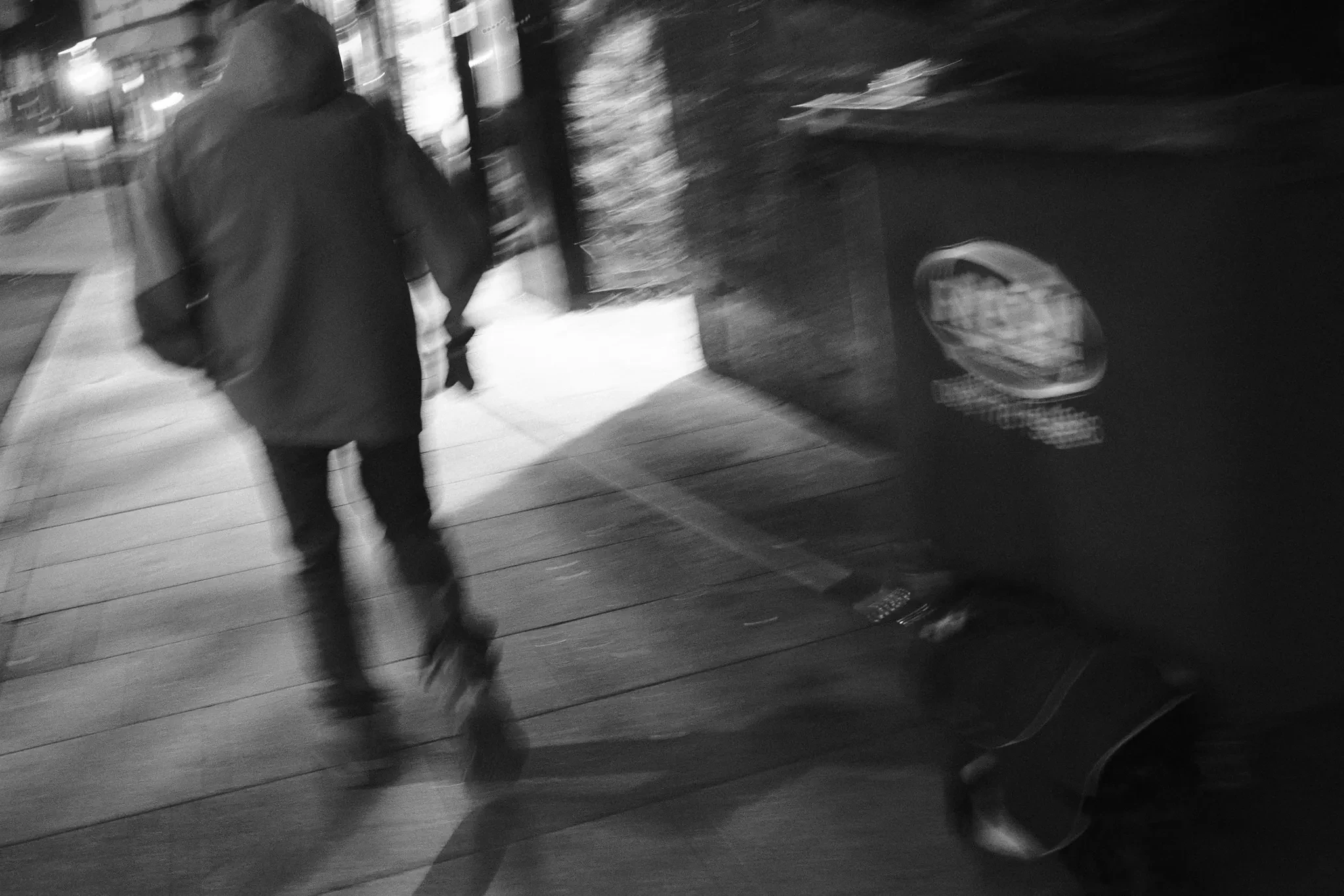 A blurred pedestrian moving past street furniture. Black and white photograph by Mark C Grant.