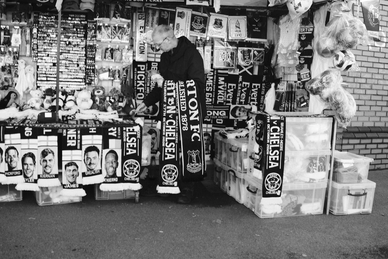 Everton scarves, shirts and printed faces fill a merchandise stall near the stadium in Liverpool. Black and white photograph by Mark C Grant.