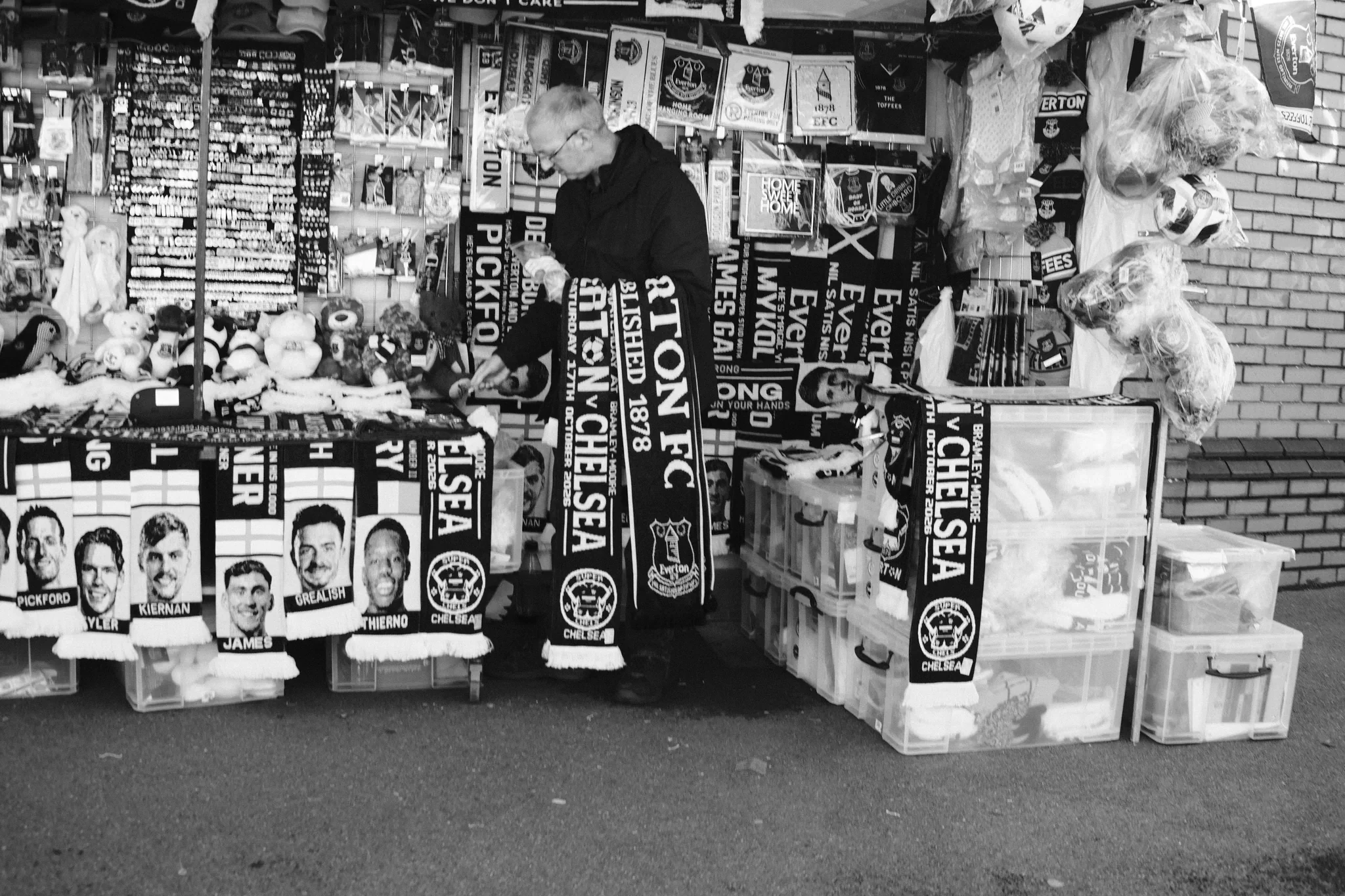 Everton scarves, shirts and printed faces fill a merchandise stall near the stadium in Liverpool. Black and white photograph by Mark C Grant.