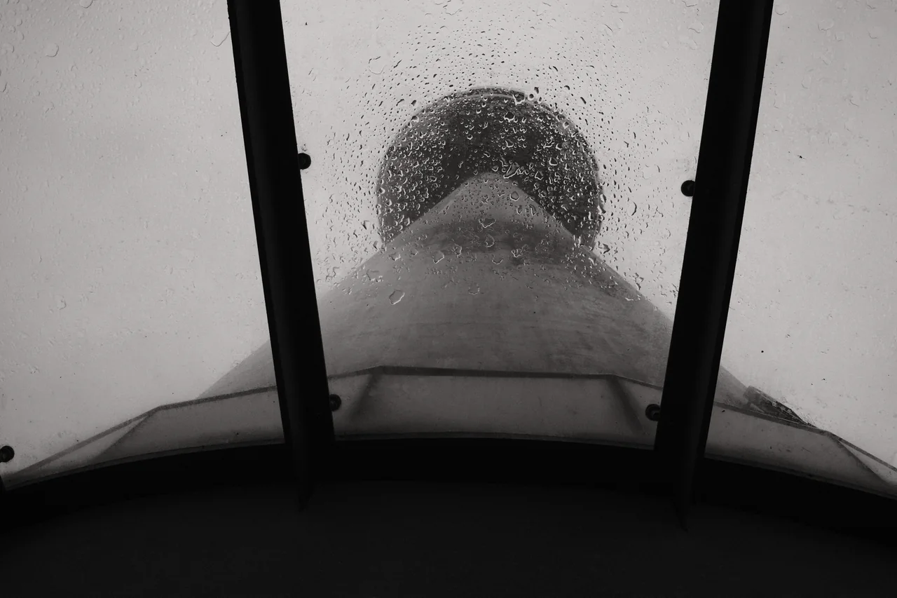 St Johns Beacon rises above a glass canopy dotted with rain, its circular crown framed by dark supports. Black and white photograph by Mark C Grant.