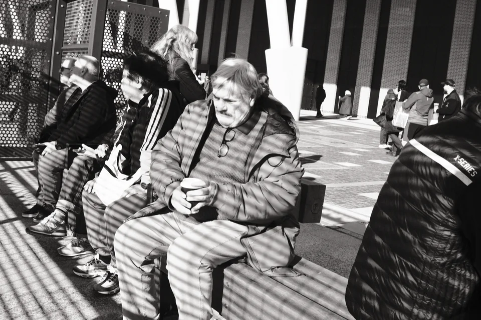 Supporters sit with drinks beneath bands of shadow outside Bramley Moore (Hill Dickinson), Liverpool. Black and white photograph by Mark C Grant.