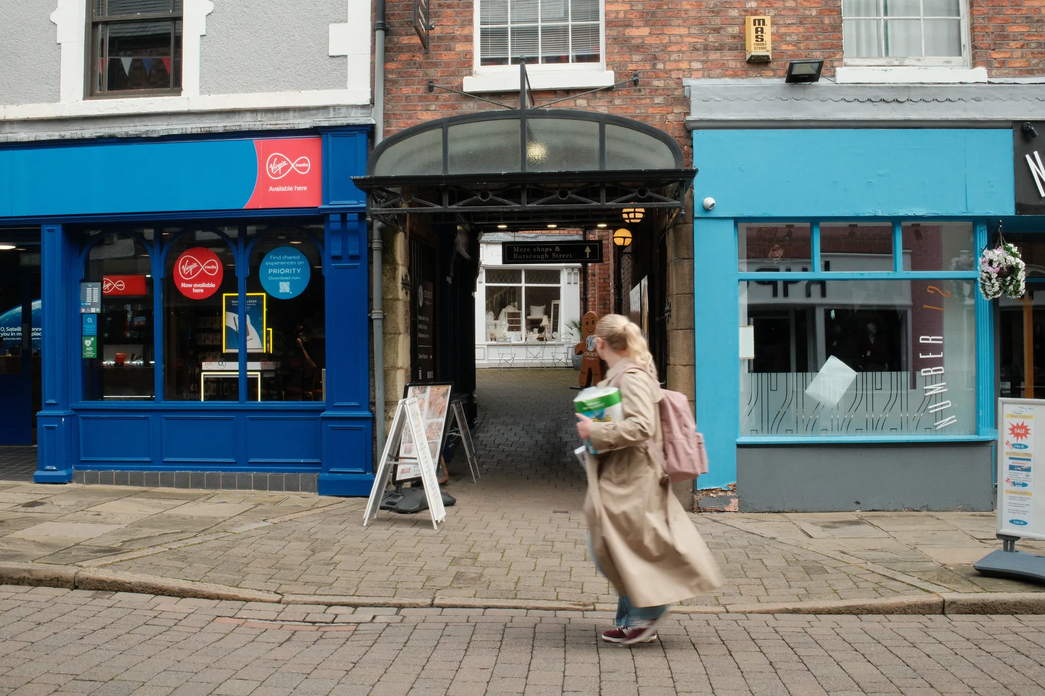 A pedestrian passes a row of bright blue shopfronts on a cobbled street.