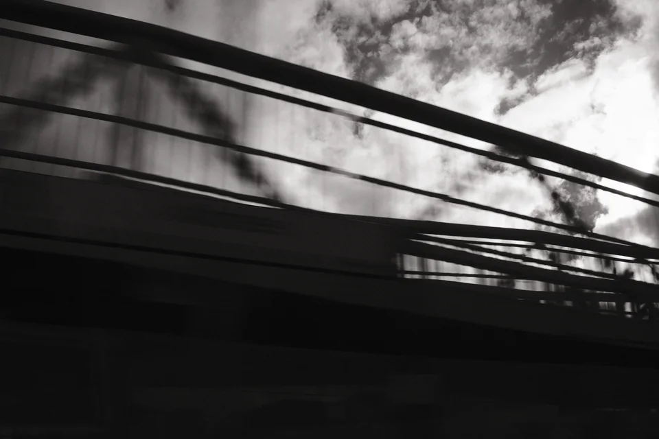 A bridge railing cuts across a blurred monochrome view of sky and trees. Black and white photograph by Mark C Grant.