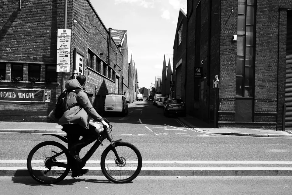 A cyclist crossing a junction between brick buildings, in black and white. Black and white photograph by Mark C Grant.