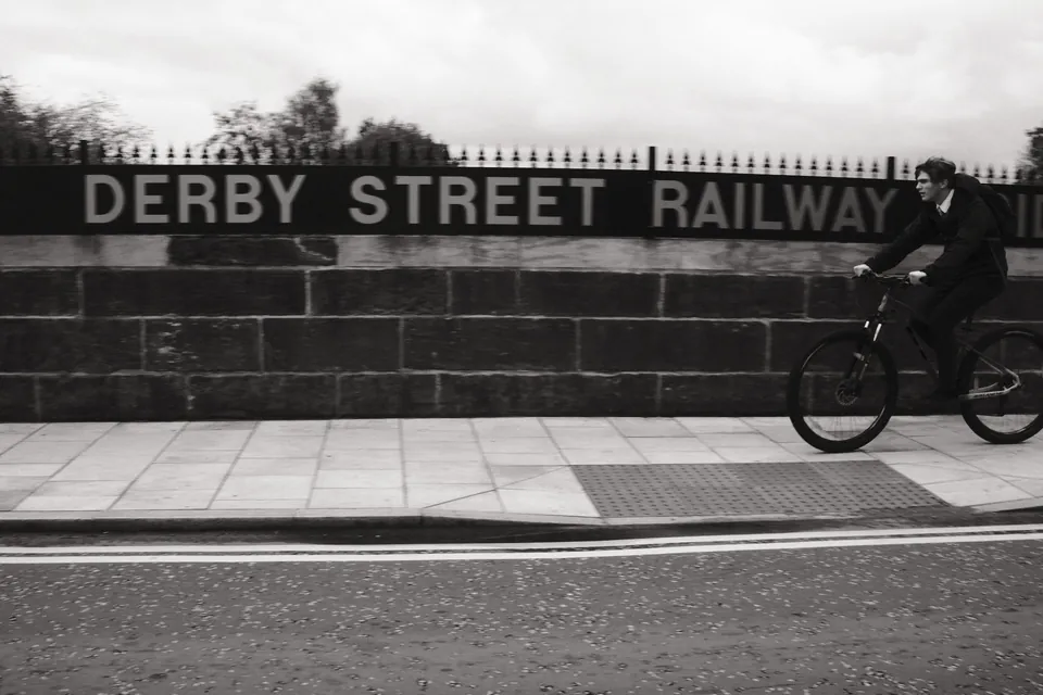 A cyclist passes the carved Derby Street Railway lettering in Ormskirk. Black and white photograph by Mark C Grant.