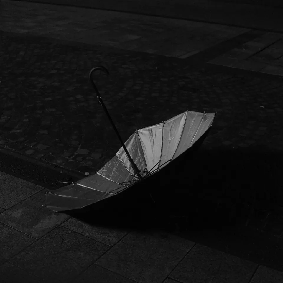 An open umbrella lying on dark paving. Black and white photograph by Mark C Grant.