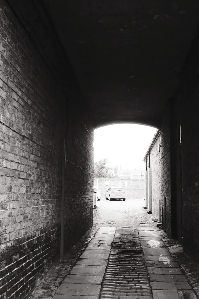 Daylight at the far end of a narrow brick passage. Black and white photograph by Mark C Grant.