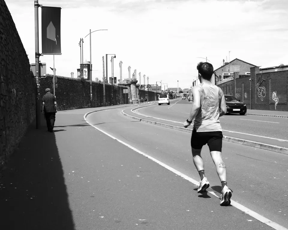 A runner following the bend of a road, photographed in black and white. Black and white photograph by Mark C Grant.