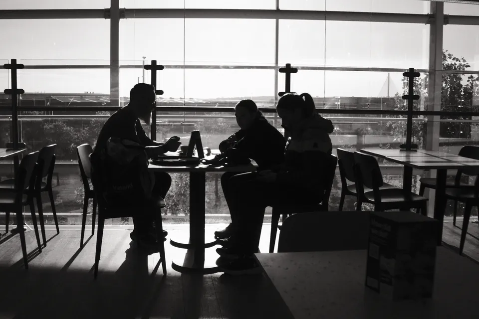 People and cafe tables appear in silhouette against broad windows. Black and white photograph by Mark C Grant.