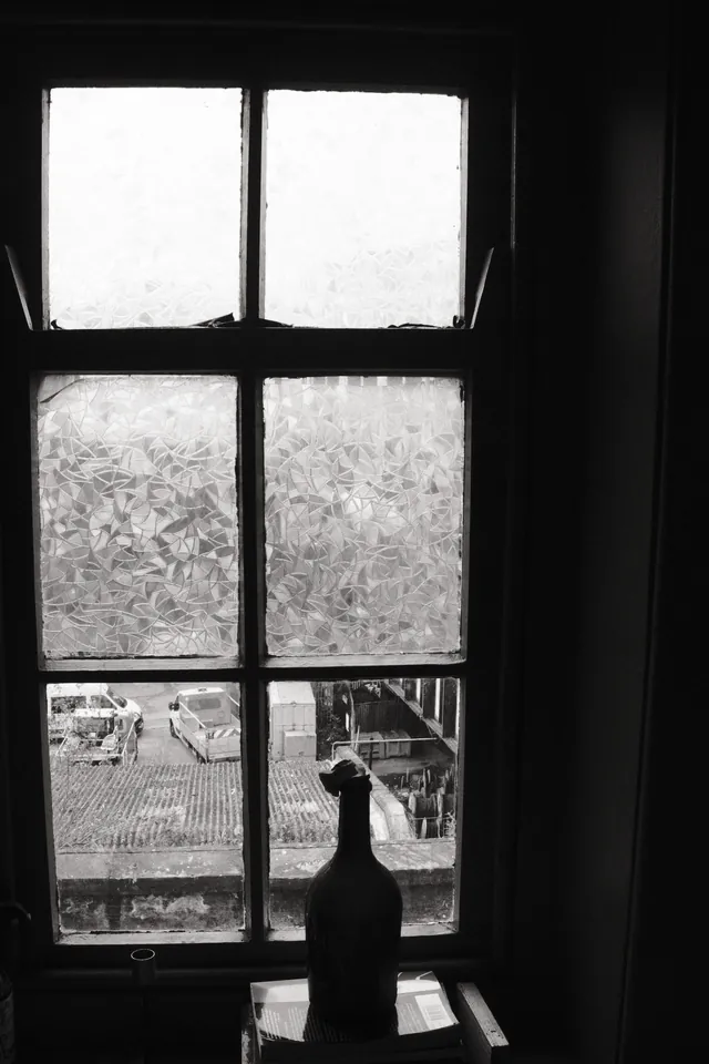A bottle-shaped silhouette rests on a sill beneath a tall divided window at the Egg Cafe, Liverpool. Black and white photograph by Mark C Grant.