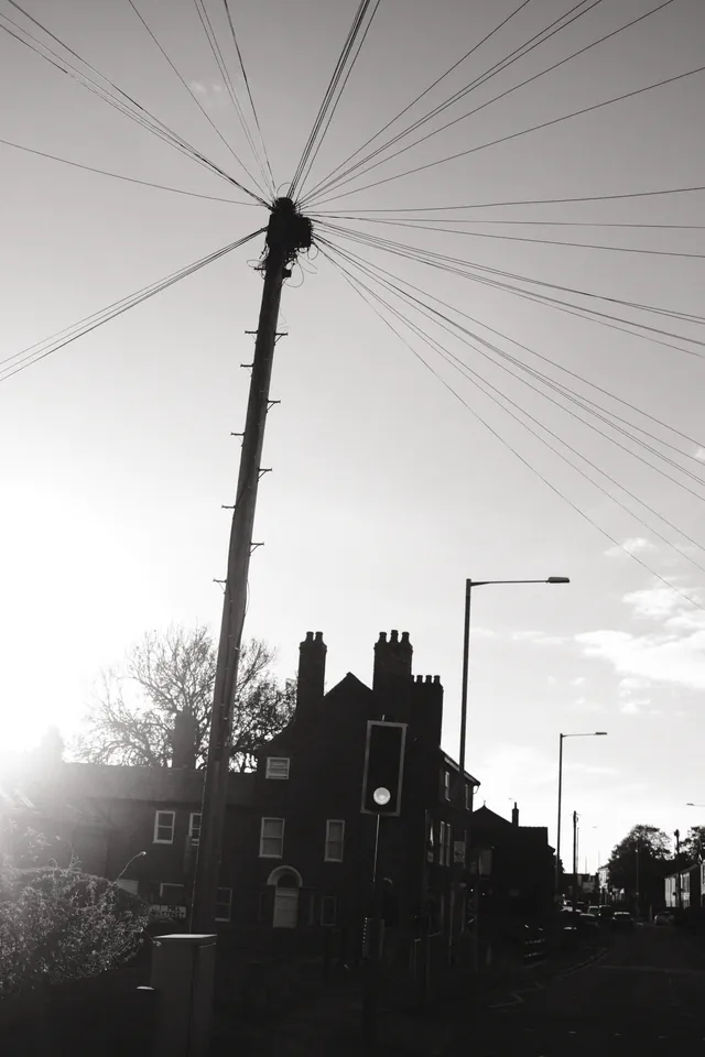 Overhead wires radiate from a pole above silhouetted rooftops near the former Windmill pub on Wigan Road, Ormskirk. Black and white photograph by Mark C Grant.