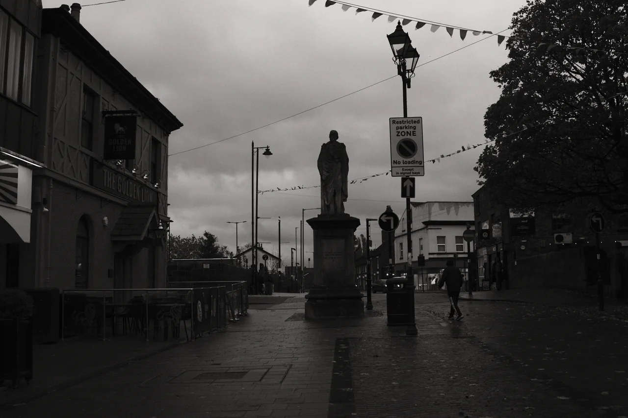 The Beaconsfield Monument stands beside the Golden Lion on rain-darkened Moor Street beneath an overcast sky. Black and white photograph by Mark C Grant.